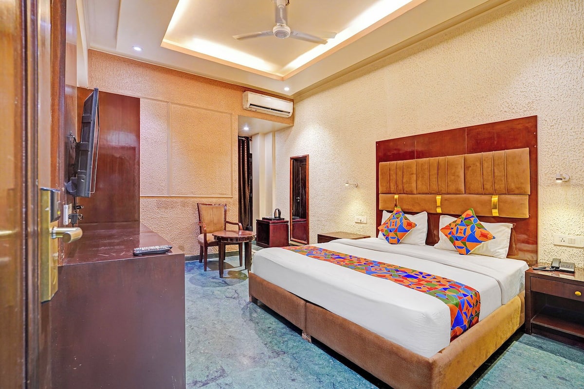 A hotel room with a large bed, a desk, a chair, and an air conditioning unit.