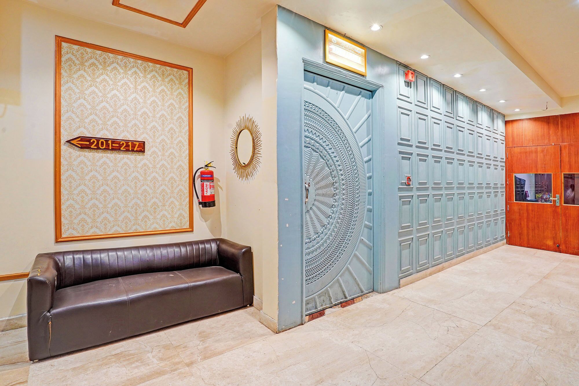 Un vestíbulo con un banco de cuero, un extintor, un muro decorativo y una puerta azul grande.