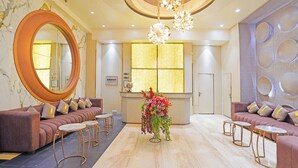 A hotel lobby with a large mirror, sofas, a reception desk, and a chandelier.
