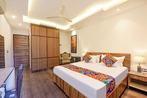 A hotel room with a bed, a desk, a chair, a wardrobe, and a ceiling fan. - Fabhotel Gracia Golf (Gurugram)