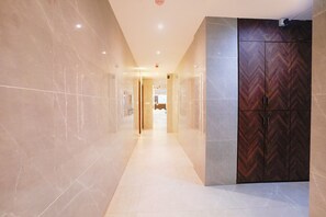 Un couloir aux murs de marbre et une porte en bois ornée d’un motif en chevrons.