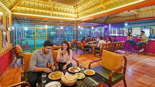 A restaurant with indoor seating, a high ceiling, and a view through large windows. - Fabhotel Arc Homes (Bhubaneshwar)