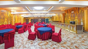 A banquet hall with round tables, red chairs, and a stage with a backdrop. - Fabhotel Arc Homes (Bhubaneshwar)
