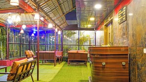 A restaurant with indoor seating, a large wooden barrel, and a view of greenery through large windows. - Fabhotel Arc Homes (Bhubaneshwar)