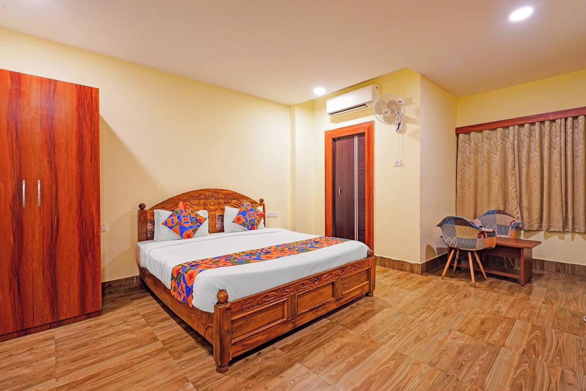 A bedroom with a wooden bed, a wardrobe, an air conditioning unit, a fan, and a window with curtains.