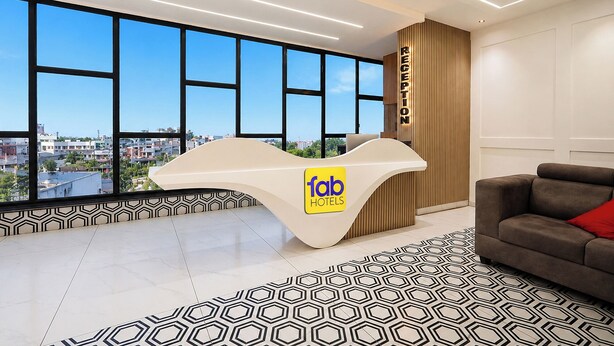 Ein Hotelrezeptionstresen mit einem Logo, ein großes Fenster mit Blick auf die Stadt, ein gemustertes Teppich und eine Couch mit einem roten Kissen.