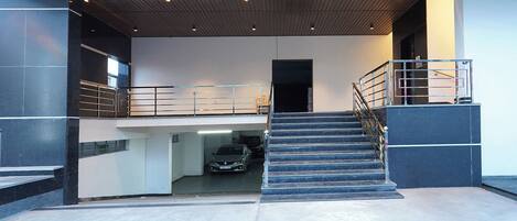 Un intérieur moderne avec un escalier menant à un niveau inférieur, une voiture garée dans un garage et une rambarde en métal à l’étage supérieur.