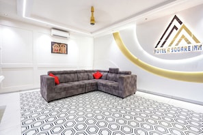 Un moderno vestíbulo de hotel con un sofá modular gris, piso estampado y un aire acondicionado instalado en la pared.