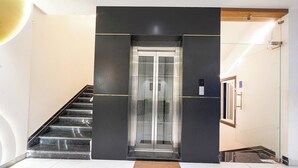 Ein moderner Aufzug mit Glastüren, eine Marmortreppe und ein aufgeräumtes, minimalistisches Interieur.