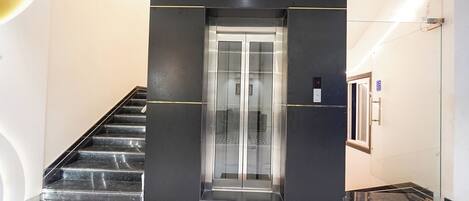 A modern elevator with glass doors, a marble staircase, and a clean, minimalist interior design.