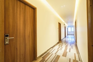 A hotel hallway with wooden doors, a patterned floor, and a bright ceiling light. - FabHotel A Square - 400m from Bhimavaram Junction (Bhimavaram)