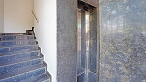 A staircase leading to a mirrored elevator, with a textured wall on the right and a plain wall on the left. - FabHotel Exotic Stay - Kalyan Nagar (Bangalore)