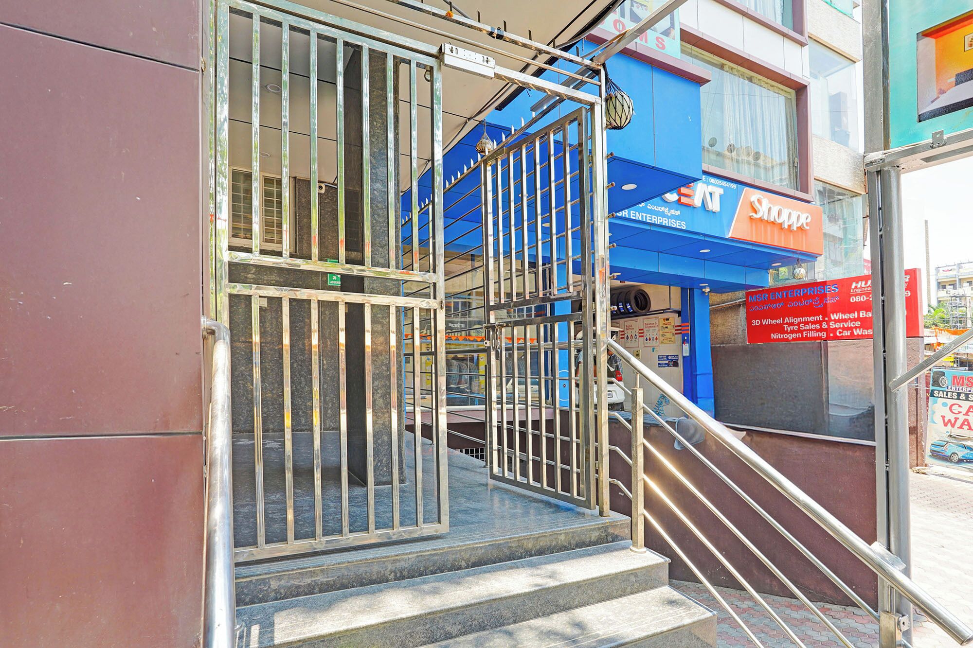 Une entrée d’immeuble avec des portails en métal, un escalier et une devanture bleue avec une enseigne.