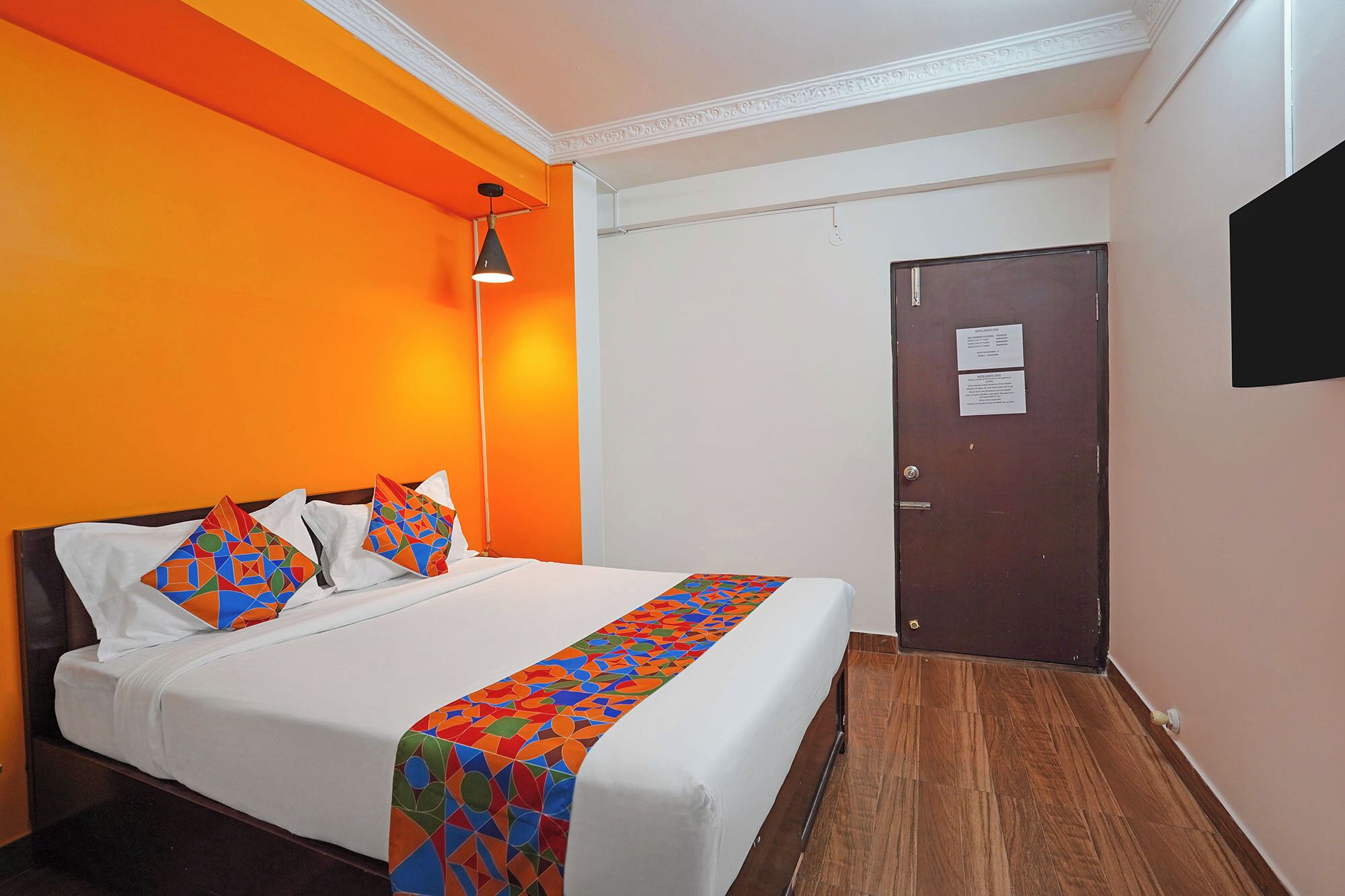 A hotel room with a bed, a nightstand, a lamp, and a door with a sign.