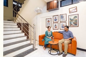 Un área de recepción con una escalera, un sofá, un ventilador y obras de arte enmarcadas en la pared.