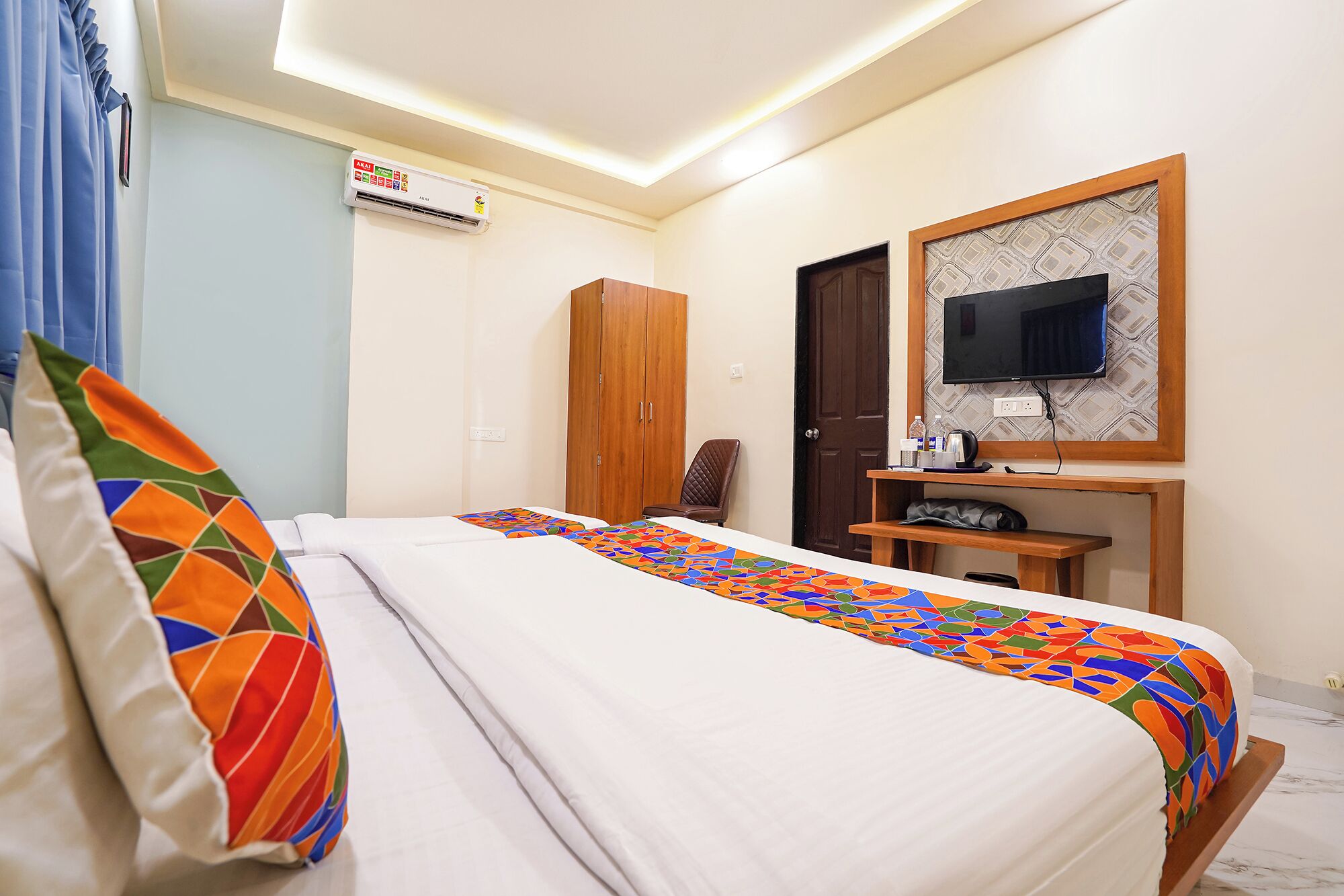 A hotel room with a bed, a desk, a chair, a television, and an air conditioning unit.
