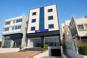 A modern hotel building with a prominent 'fob hotels' sign, a staircase leading to the entrance, and a signboard advertising 'Sunrise Comfort Rooms' with amenities like hot water. - Fabhotel Sunrise Comforts (Pune)