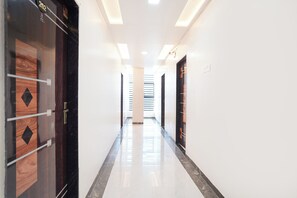 A corridor with a polished floor, a door with a number plate, and a wall with a light switch. - Fabhotel Sunrise Comforts (Pune)