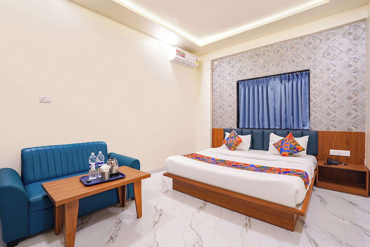 A hotel room with a bed, a blue sofa, a wooden side table, and a patterned wall.