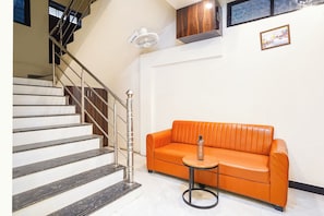 A staircase with metal railings, an orange leather sofa, a small round table, and a wall-mounted fan. - Fabhotel Sunrise Comforts (Pune)