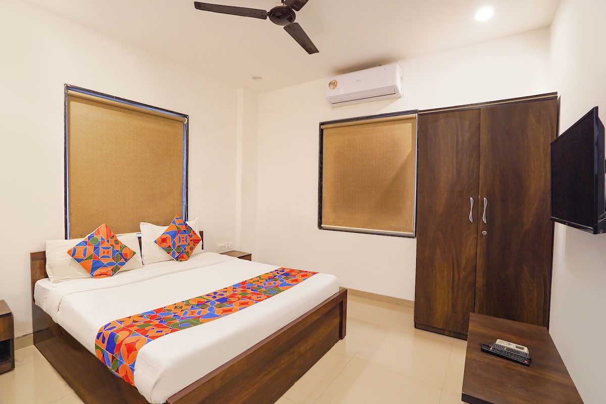 A hotel room with a bed, a wardrobe, a TV, and an air conditioning unit.