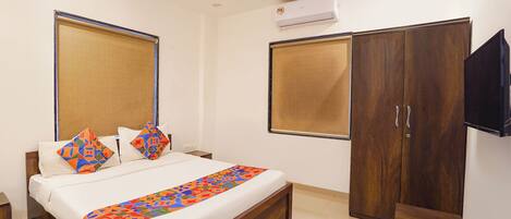 A hotel room with a bed, a wardrobe, a TV, and an air conditioning unit.