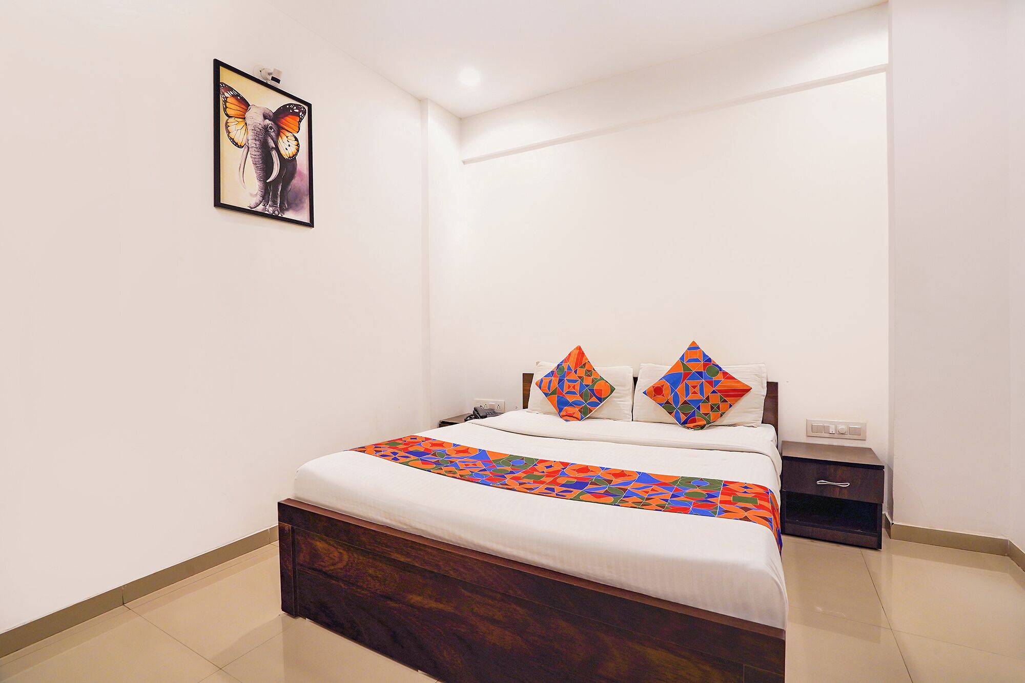 A bedroom with a bed, pillows, a nightstand, a drawer, and a wall-mounted picture.