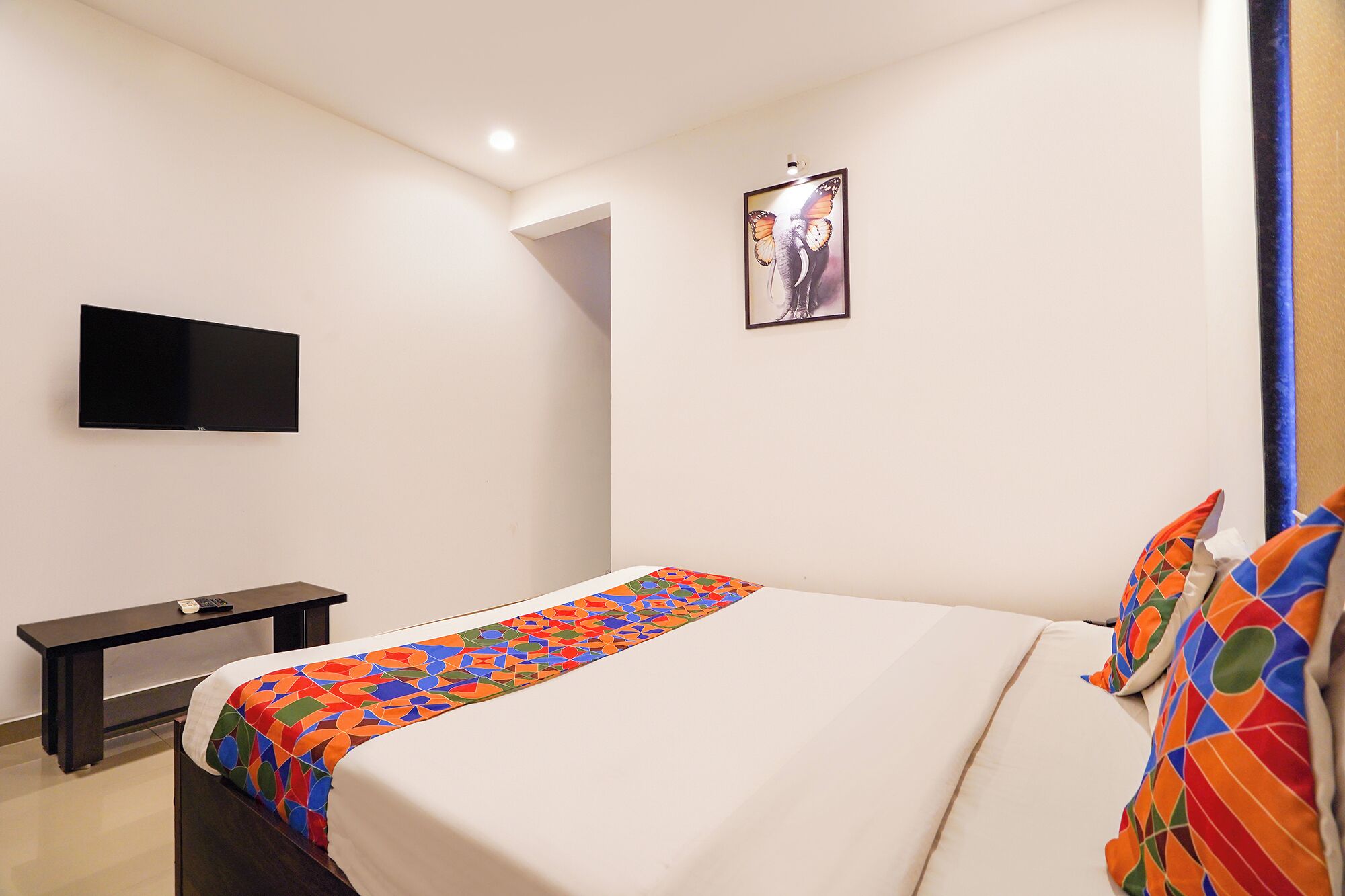 Habitación de hotel con cama, televisión de pantalla plana, un escritorio pequeño y un cuadro en la pared.