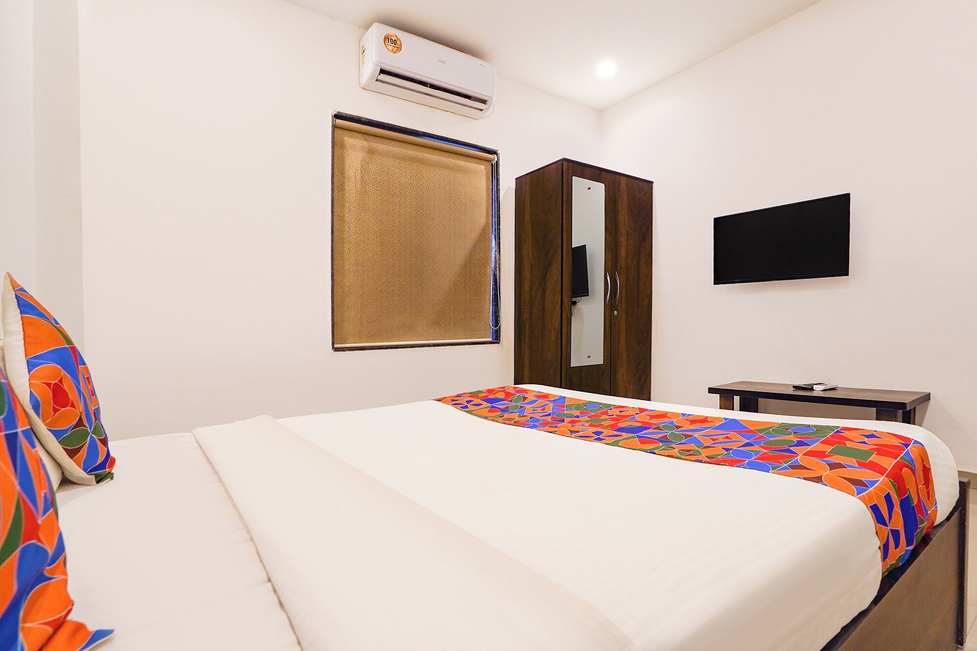 A hotel room with a bed, a TV, a wardrobe, and an air conditioning unit.