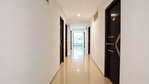 A long, narrow hallway with a reflective floor, doors on both sides, and a bright window at the end. - Fabhotel Rvc Hospitality (Pune)