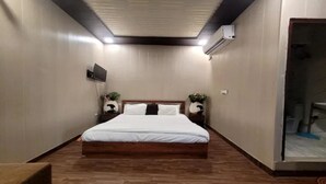 A hotel room with a wooden floor, a bed with white bedding, a TV mounted on the wall, and an air conditioning unit. - Fabhotel Blest Inn (New Delhi)