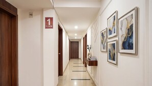 Un pasillo de hotel con un cartel que indica '1 PISO', una puerta de madera a la izquierda y obras de arte enmarcadas en la pared derecha.