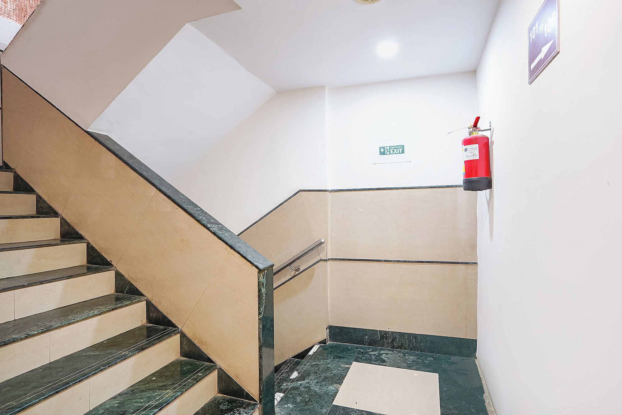 A staircase with beige and green marble steps, a metal handrail, and a red fire extinguisher on the wall.