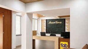 Un mostrador de recepción con una computadora portátil y un monitor, un letrero que dice 'Arusai Homes' y un rótulo que indica 'fab Hotel'.
