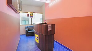 Un mostrador de recepción de hotel con un letrero de 'fab hotels', piso alfombrado en azul, un ventilador de techo y una ventana con vistas.