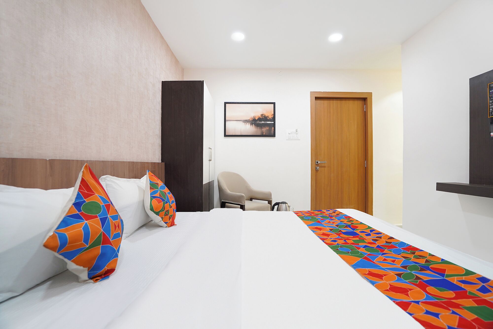 Una camera d'albergo con un letto, una sedia, una porta in legno e un quadro appeso al muro.
