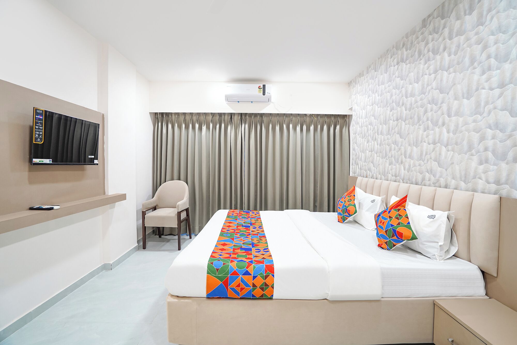 Ein Hotelzimmer mit Bett, Sessel, Fernseher und Wandklimaanlage.