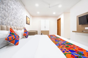A hotel room with a bed, pillows, a wall-mounted TV, a wardrobe, and a coffee maker.