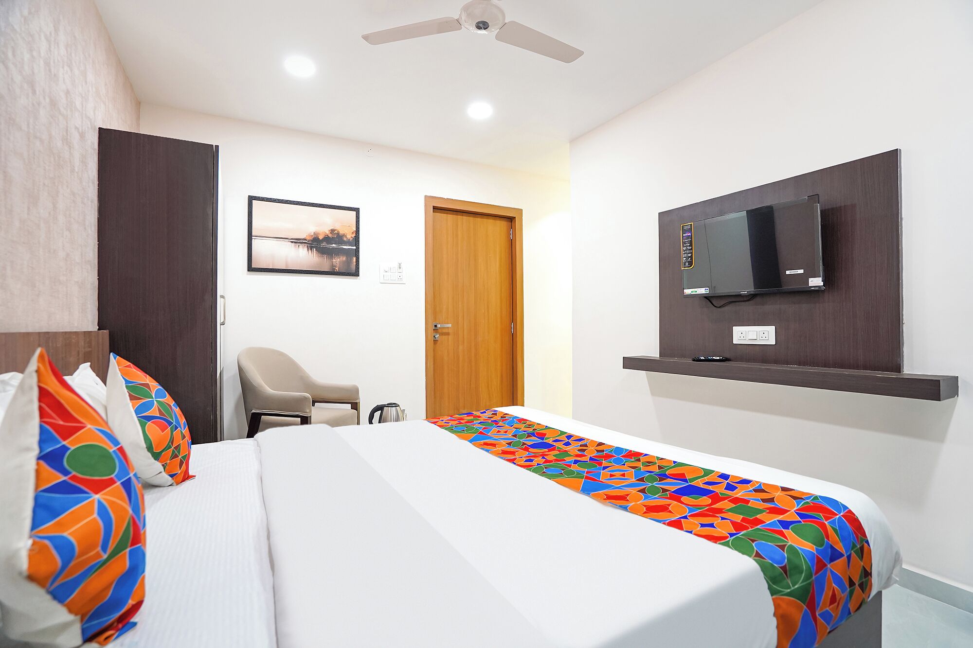 A hotel room with a bed, a chair, a television mounted on the wall, and a door.