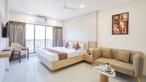 A hotel room with a bed, a sofa, a TV, a ceiling fan, and a painting on the wall. - Fabhotel Sahyadri Mantram (Pune)