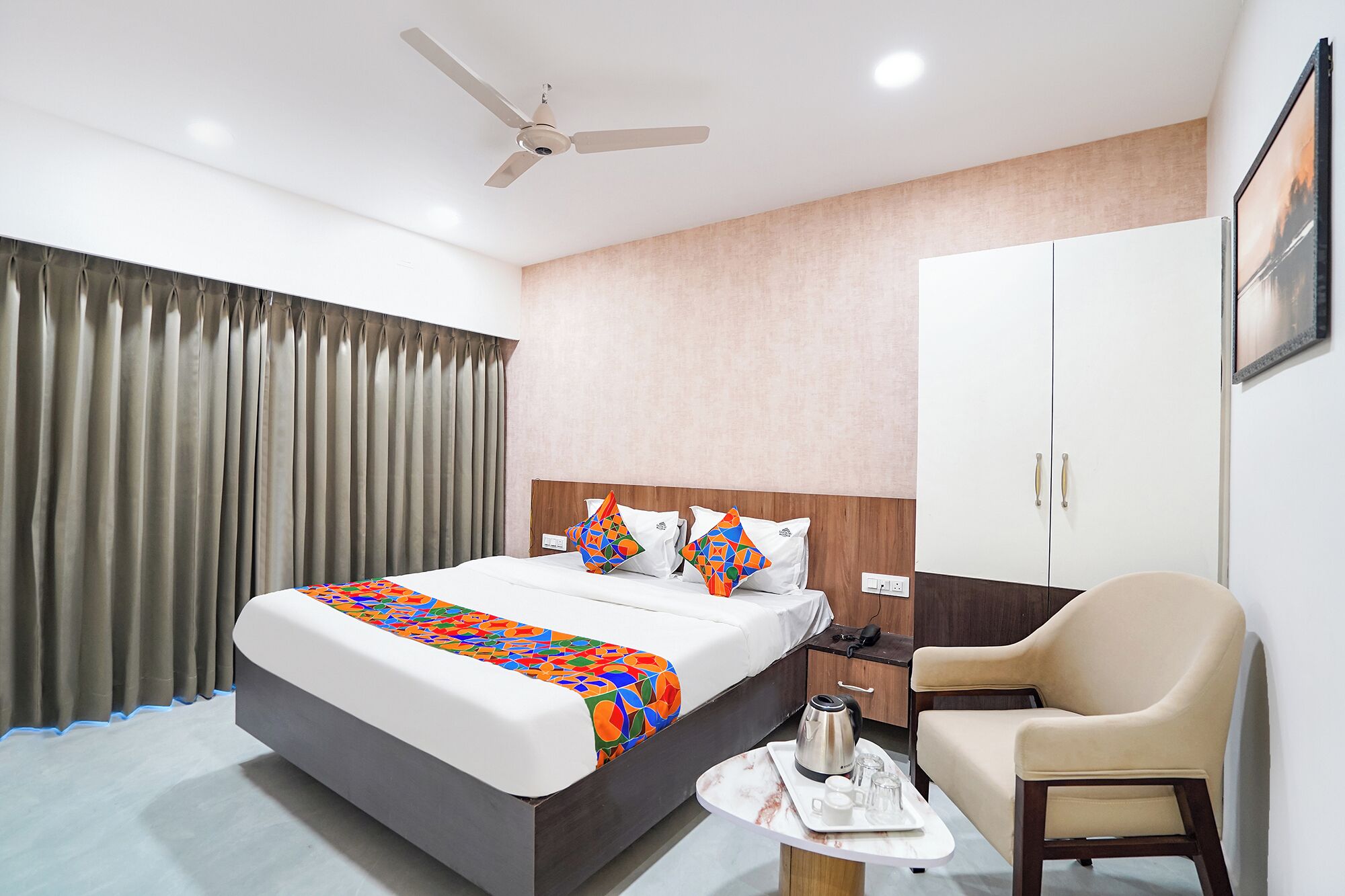 A hotel room with a bed, a chair, a desk, a coffee maker, and a ceiling fan.