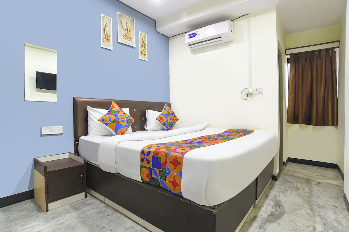 A hotel room with a bed, a nightstand, a wall-mounted air conditioner, and a window with curtains.