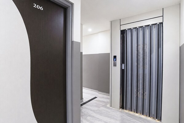 A modern elevator with a digital display, a dark door with the number 206, and a metallic wall with perforated panels. - FabHotel BR Green (Indore)
