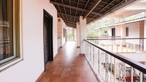 Ein Korridor mit Fliesenboden, ein Balkon mit weißen Geländern und ein überdachter Bereich mit Holzboden.