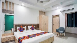 A bedroom with a bed, a chair, a wardrobe, and an air conditioning unit. - FabHotel Prime IJ Suites - Kasavanahalli (Bangalore)