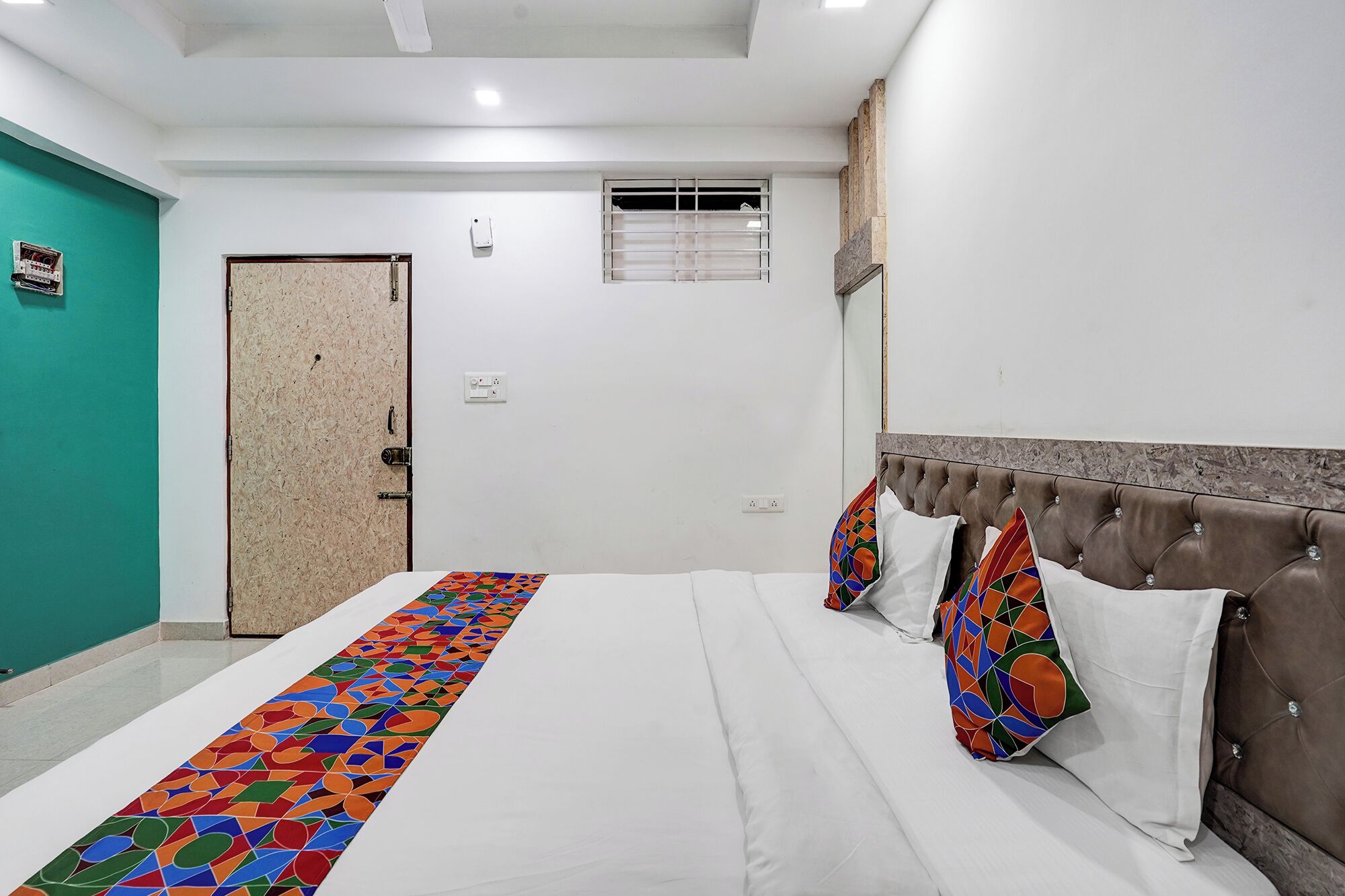 A hotel room with a bed, a door, a window, and a wall-mounted air conditioning unit.