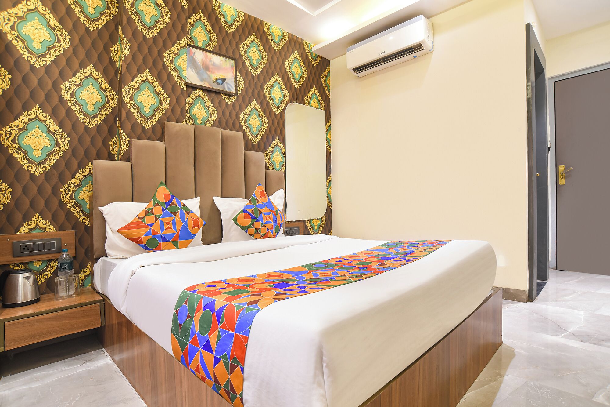 Una habitación de hotel con cama, mesita de noche, equipo de aire acondicionado y puerta.