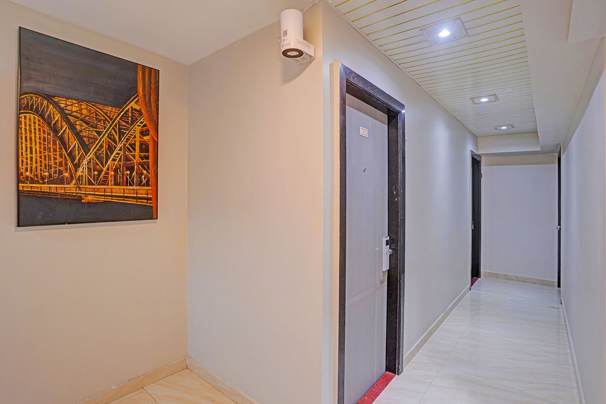 A hallway with a painting of a bridge, a white ceiling with recessed lighting, and a door with a number.