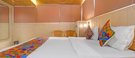A hotel room with a wooden ceiling, a bed with white linens, two wooden chairs, and a colorful geometric-patterned throw.
