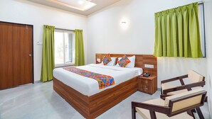 A bedroom with a wooden bed, green curtains, a ceiling fan, and a bedside table with a phone. - Fabhotel Nakshtra Resort (Tasgaon)
